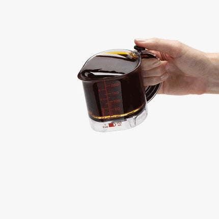 4-in-1 Adjustable Measuring Cup Hand holding a glass measuring cup filled with dark liquid on a white background