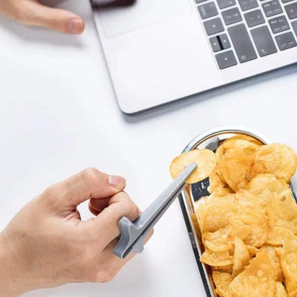 Snack Grabbers. Person using a smartphone with a transparent stand on a desk next to a container of chips and a laptop.