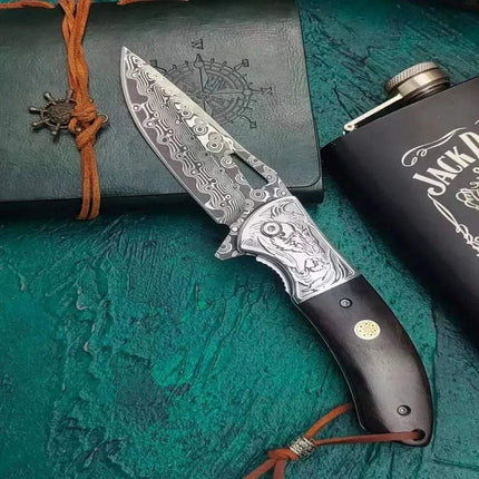 Damascus Steel Pocket Knife Camping & Craft Tool on textured background with flask and notebook.
