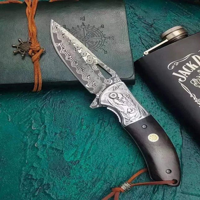 Damascus Steel Pocket Knife Camping & Craft Tool on textured background with flask and notebook.