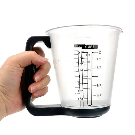 Hand holding a Digital Measuring Cup with black handle and measurement markings on a white background. Astoria Lifestyle