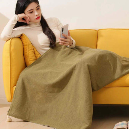 Woman sitting on a yellow couch using a phone with a green Wearable Electric Heating Blanket draped over her legs.
