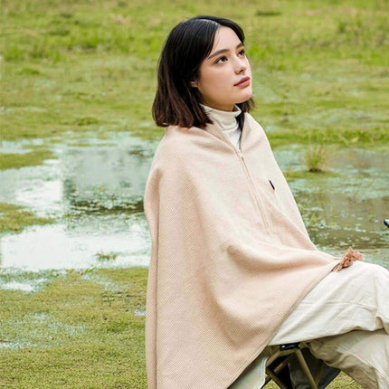 Woman sitting on a chair in a grassy field wearing a Wearable Electric Heating Blanket.