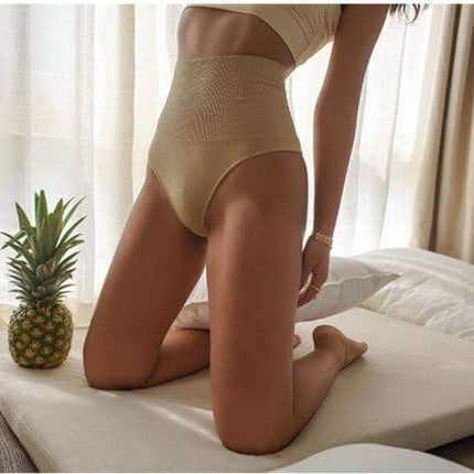 A lady wearing beige Women Slimming Thong Shapewear for Tummy Control sitting on a bed with a pineapple and white curtains in the background.