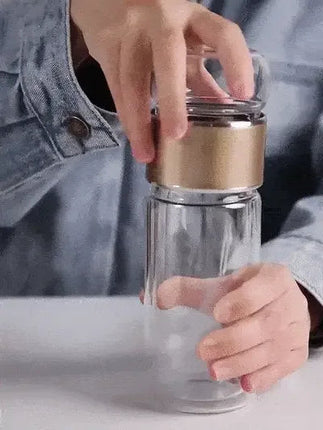 Hands using a Tea Infuser Bottle with a gold band, showcasing its elegant design for hot and cold brewing.