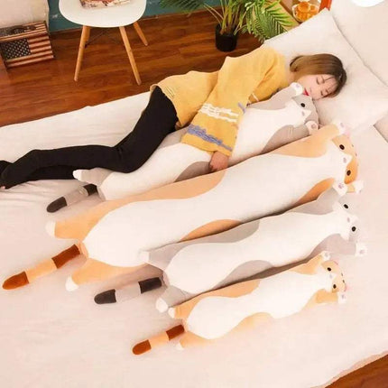 Person lying on a bed with large plush  Long Cat Pillow