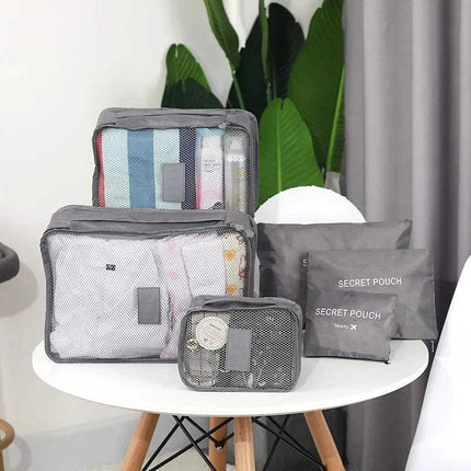 Set of gray 6Pcs Travel Clothes Storage Bags on a white table with plants in the background