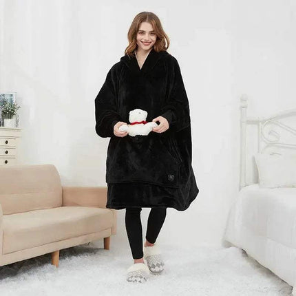 Woman wearing a black Oversized Heatable Hoodie holding a white teddy bear in a bedroom setting.