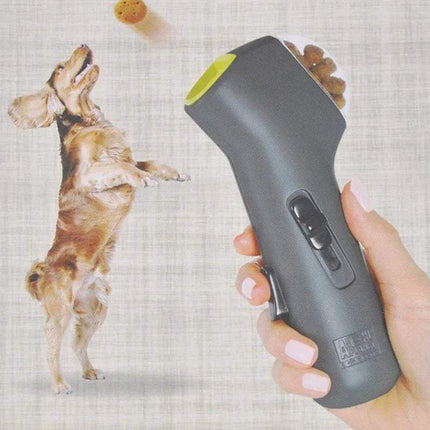 Hand holding a gray and green Dog Treat Launcher Interactive Training & Play Toy with a dog in the background
