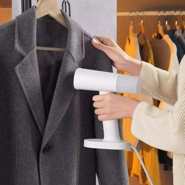 Person using a Handheld Garment Steamer on a gray coat with a blurred clothing store background.