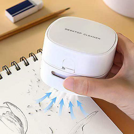 Hand holding a white Mini Vacuum Cleaner For Table Compact 360° Desk Cleaning Solution over a notebook with cleaning action illustrated.