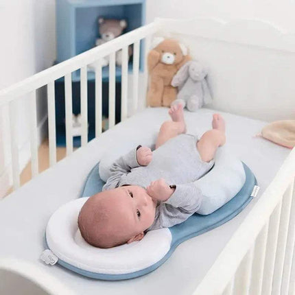 Baby lying on a white and blue Baby Anti-Rollover Sleeping Pillow in a crib with teddy bears in the background