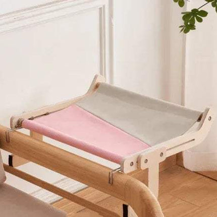 Sturdy Hanging Cat Bed with a gray & pink cushion in a room with white walls and a plant.