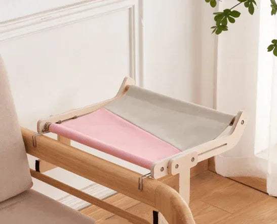 Sturdy Hanging Cat Bed with a gray & pink cushion in a room with white walls and a plant.