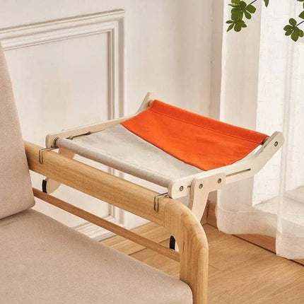 Sturdy Hanging Cat Bed with orange and gray cushion attached to a sofa in a room with white walls and a plant.