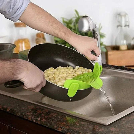 Person washing vegetable in a pan with a green Universal Silicone Strainer Clip over a sink.
