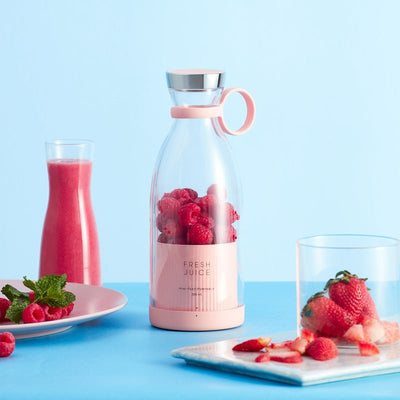 Pink juice carafe with raspberries, glasses of juice, and plates of strawberries on a blue background