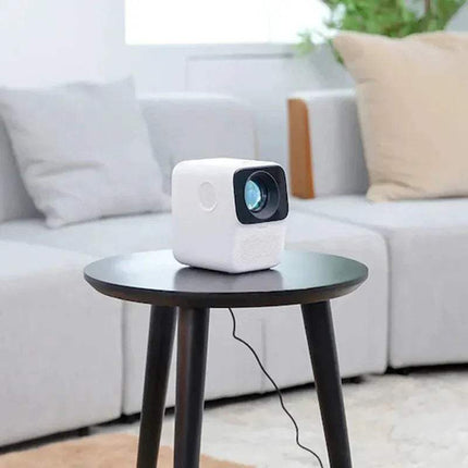 White portable WANBO T2 Max Projector 1080P on a small round table in a living room setting.