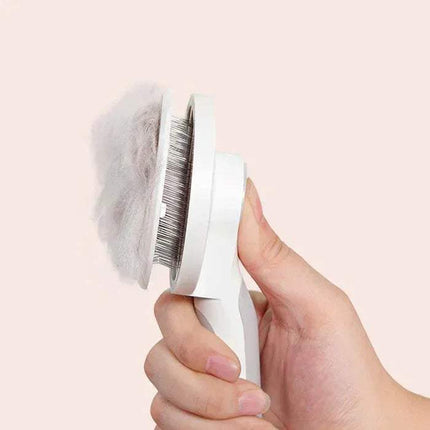 Hand holding a Self-Cleaning Pet Brush Gentle Grooming & Undercoat Removal with pet hair on a light pink background