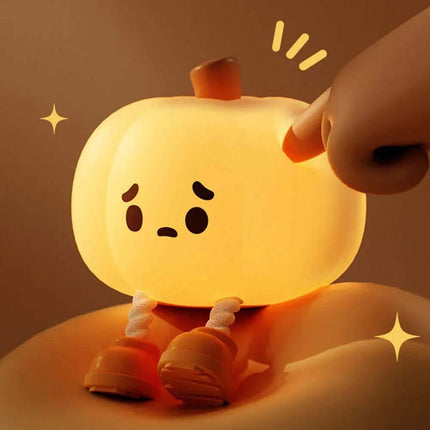 Cute Pumpkin Night Light with a hand interacting with it on a warm brown background.